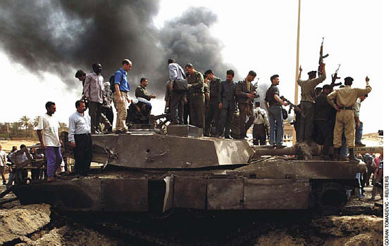 Iraqi soldiers stand on top of a destroyed US tank in the southern outskirts of Baghdad